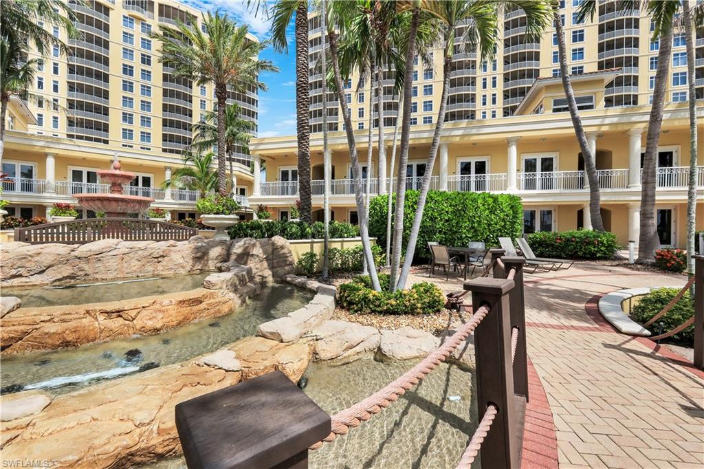 Resort-style courtyard featuring a multi-tiered rock water feature, mature palm trees, paved walkway, and private cabanas