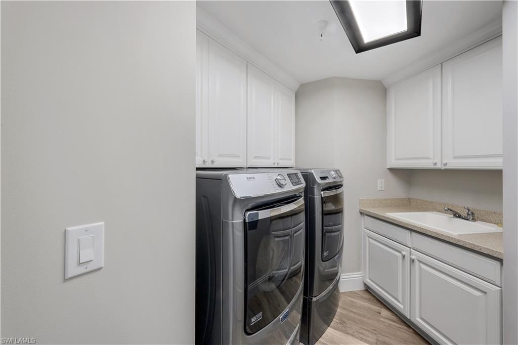 Dedicated laundry room featuring wood-finish flooring, light grey walls, white shaker-style cabinetry, a built-in utility sink, and a light-colored countertop