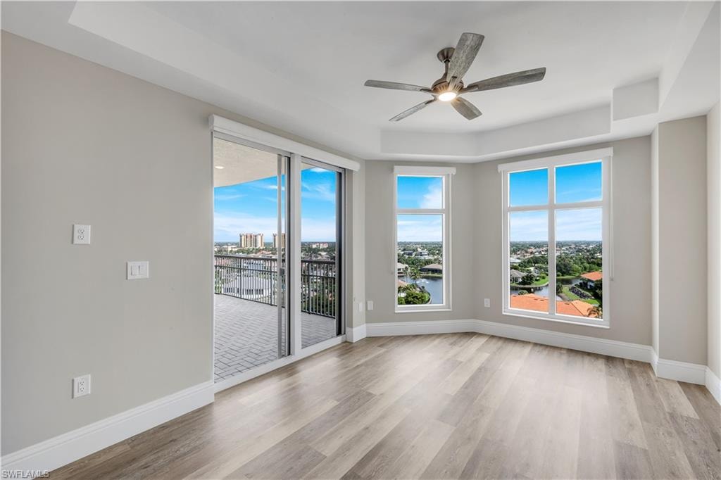 Bedroom #3 featuring wood-finish flooring, a tray ceiling with a ceiling fan, and large windows
