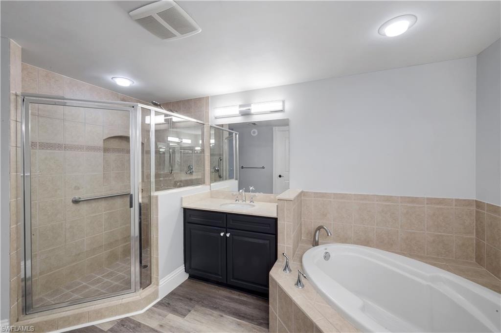 Primary bathroom featuring a glass-enclosed shower, a built-in soaking tub, a dark wood-finish vanity with a light-toned countertop, and wood-finish plank flooring