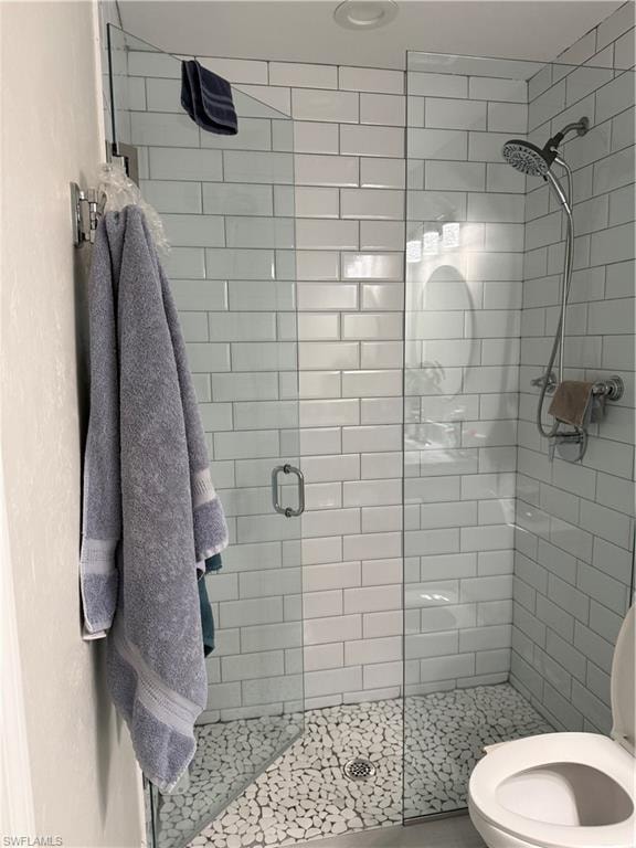 Full glass shower enclosure featuring white subway tile surround and a pebble stone shower floor