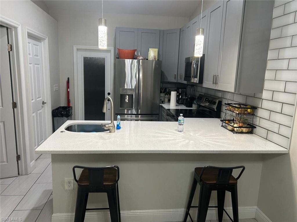 Kitchen featuring light gray cabinetry, white subway tile backsplash, stainless steel appliances, and a white countertop island with an undermount sink and gooseneck faucet