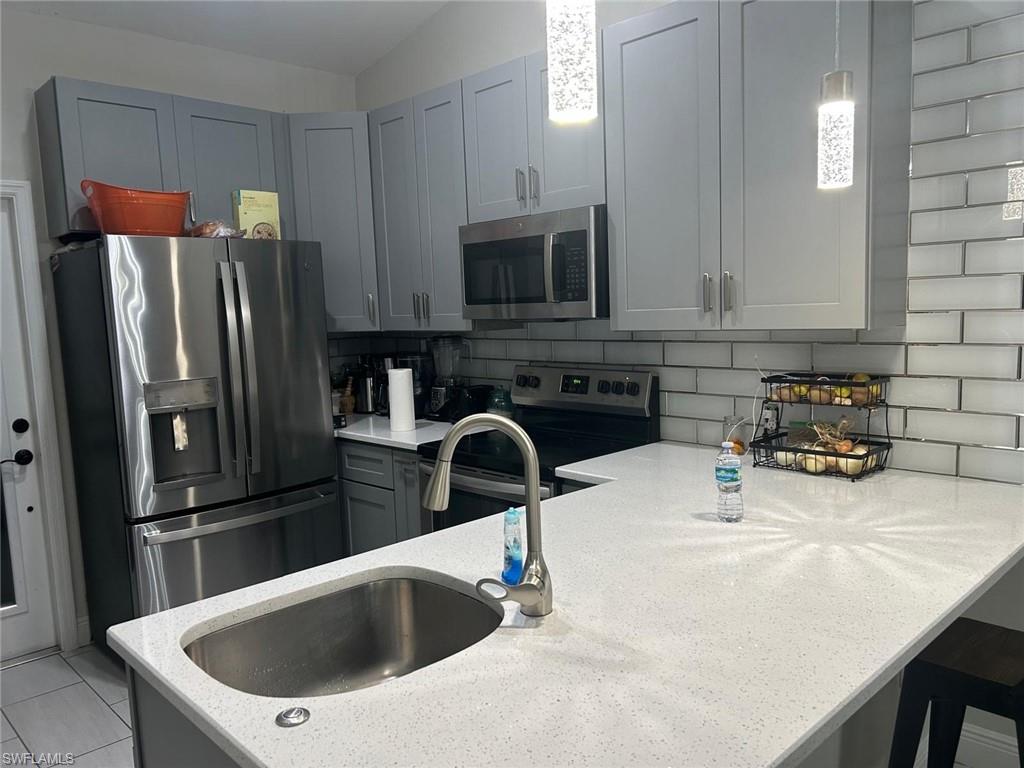 Kitchen featuring light gray cabinetry, stainless steel appliances, white subway tile backsplash, and light-colored countertops with an undermount sink