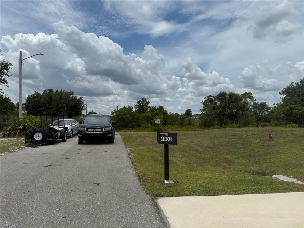 Expansive grass lot featuring a mailbox with visible numbers, paved street access, and a concrete apron