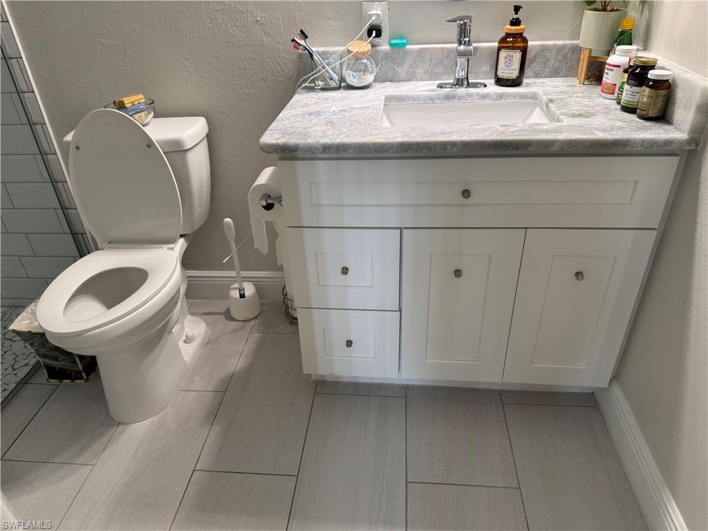 Bathroom featuring a white vanity with shaker-style cabinetry, a gray patterned countertop, an undermount sink with a chrome faucet, and rectangular tile flooring