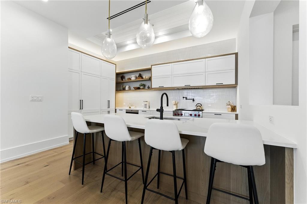 Kitchen featuring decorative backsplash, light countertops, open shelves, a breakfast bar, and white cabinetry