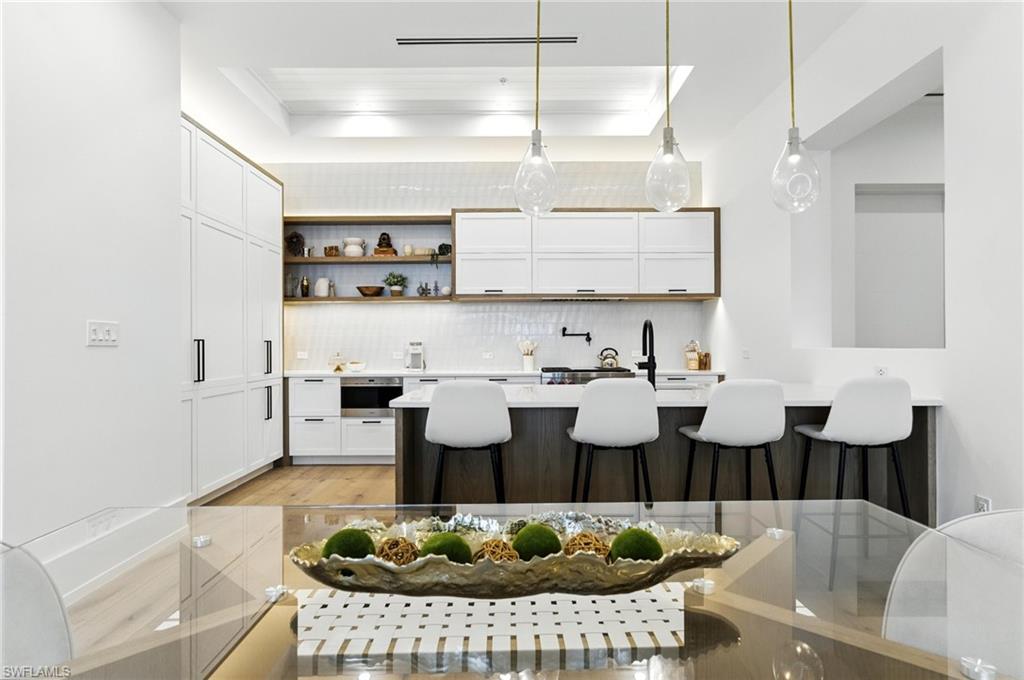 Kitchen with tasteful backsplash, a breakfast bar, light countertops, white cabinetry, and light wood finished floors