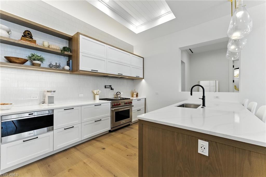 Kitchen featuring designer range, light wood-style floors, tasteful backsplash, white cabinets, and light stone counters