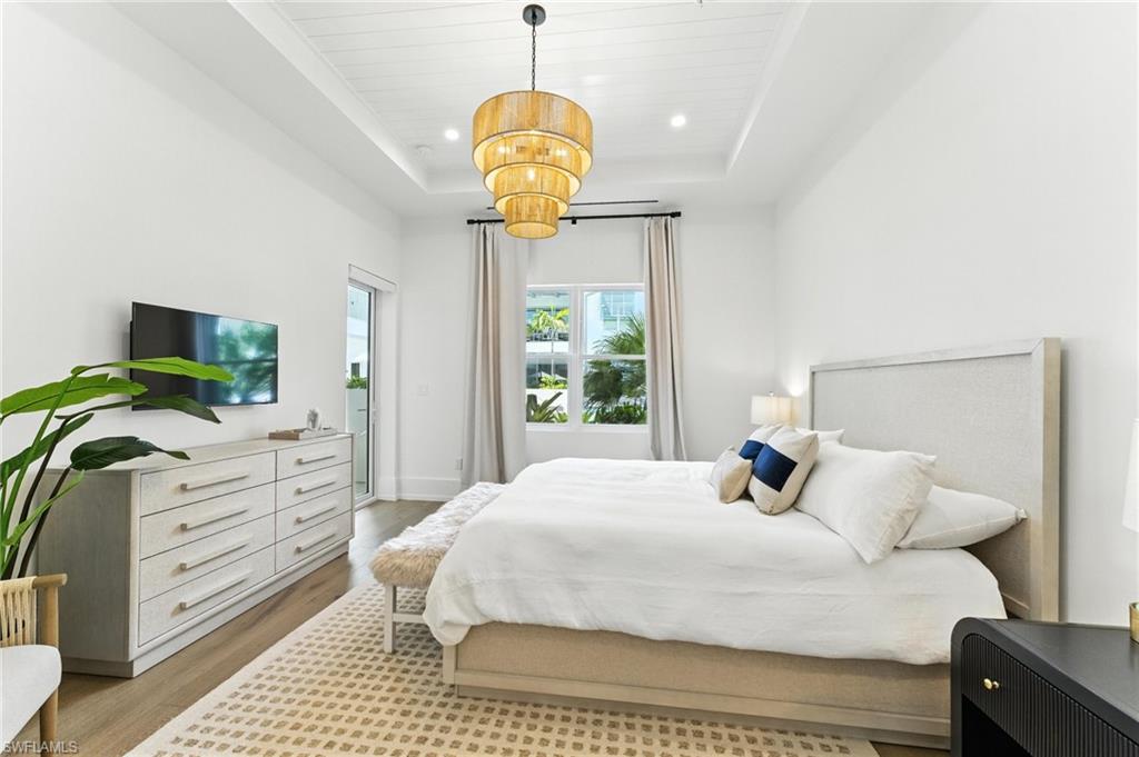 Bedroom featuring a tray ceiling, light wood finished floors, a chandelier, recessed lighting, and access to exterior, IMPACT WINDOWS AND DOORS, 2 walk-in closets in hallway