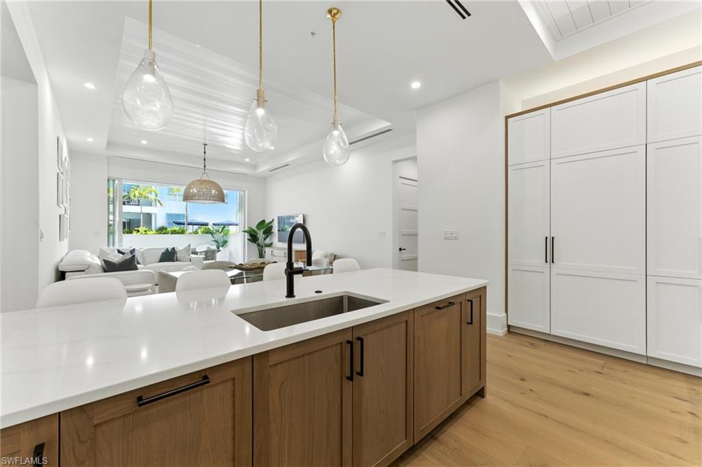 Dining room with bar with sink, light wood-style floors, recessed lighting, and a tray ceiling