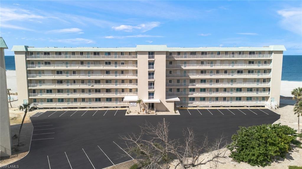 Beachfront multi-story building featuring multiple private balconies, a large parking area, and direct beach access