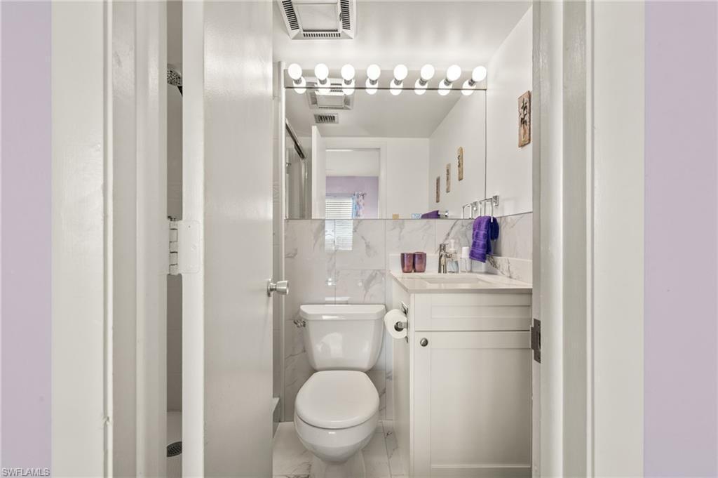 Compact bathroom featuring a white vanity with a light-toned countertop, a large mirror with integrated lighting, and white tile wainscoting