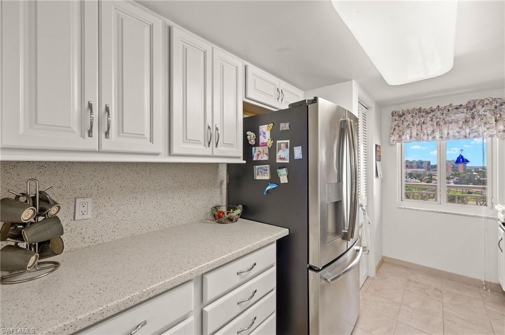 Kitchen featuring white shaker-style cabinetry, light speckled countertops, a matching backsplash, and tile flooring
