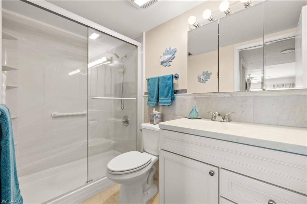 Bathroom featuring a glass-enclosed shower with grab bar, white vanity with integrated sink, dual medicine cabinets, and a three-bulb vanity light fixture