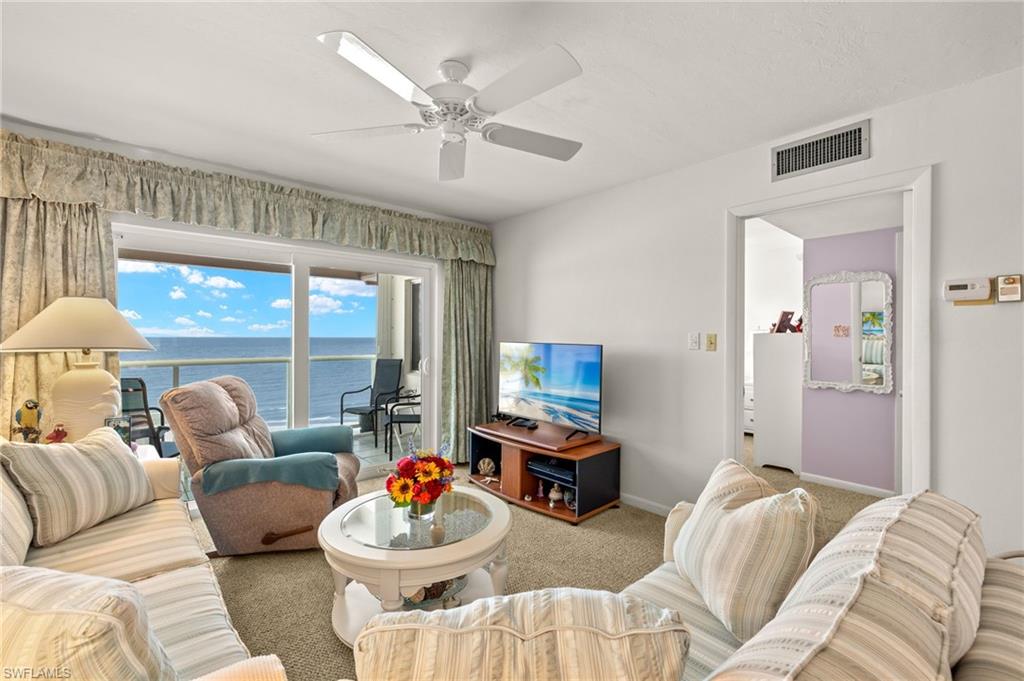 Living area featuring direct water scenery through expansive glass sliders, ceiling fan, and light-toned carpeting