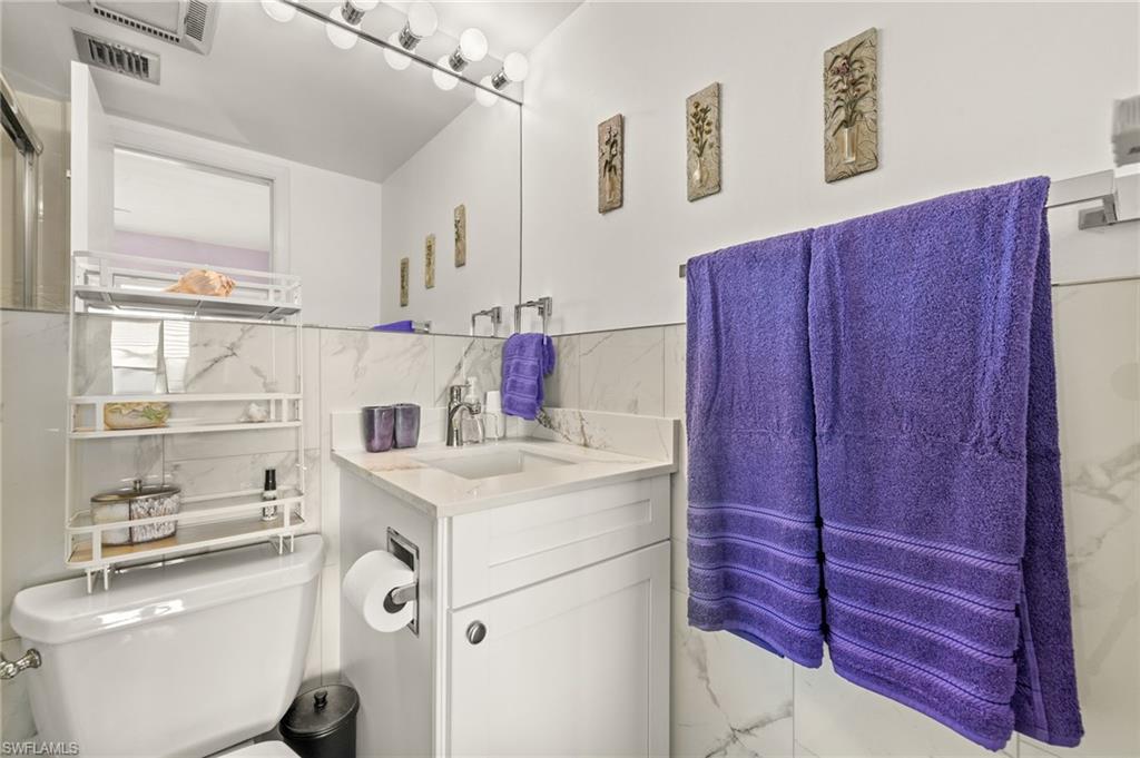 Bathroom featuring white marble-look wall tiling, a white vanity with an integrated sink, a large wall-mounted mirror, and overhead vanity lighting