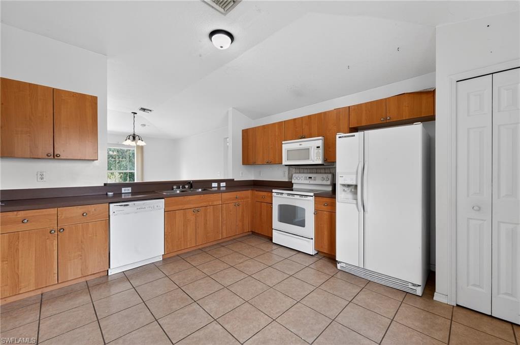 Expansive kitchen featuring wood cabinetry, white appliances, dark countertops, and tile flooring