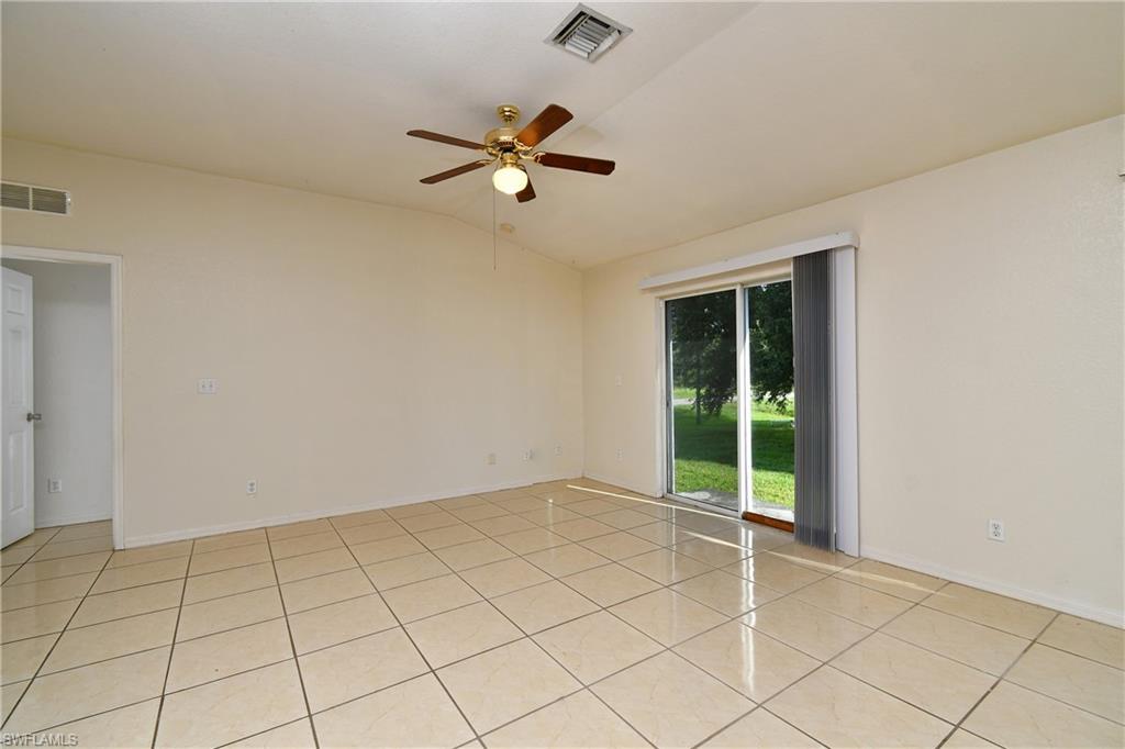 Spacious interior room featuring light-toned tile flooring, vaulted ceilings, and a ceiling fan with integrated lighting