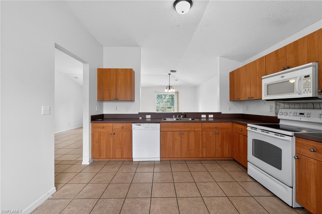 Kitchen featuring a white appliance suite, wood cabinetry, and a dark countertop