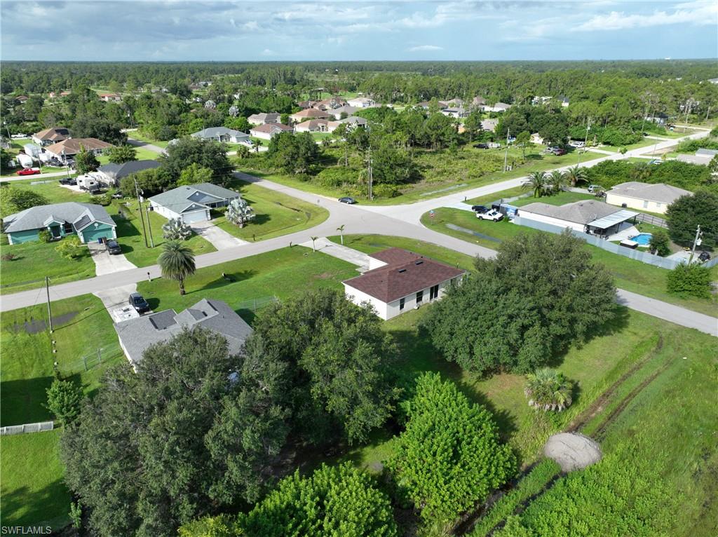 Aerial perspective of a residential area featuring multiple single-story homes, established landscaping, paved streets, and a backdrop of abundant mature trees