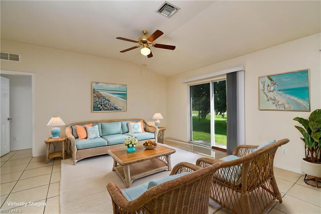 Vaulted ceiling living area featuring tile flooring, ceiling fan with light fixture, and sliding glass doors providing outdoor access