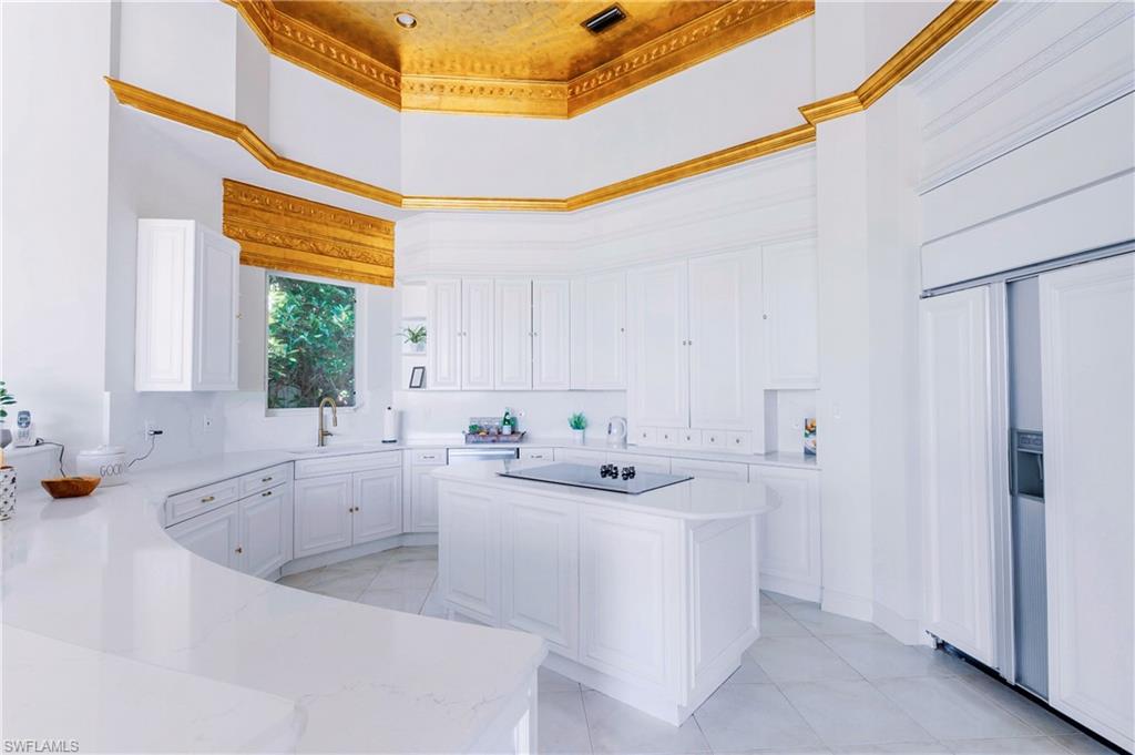 Kitchen with a kitchen island, sink, a high ceiling, ornamental molding, and white cabinets