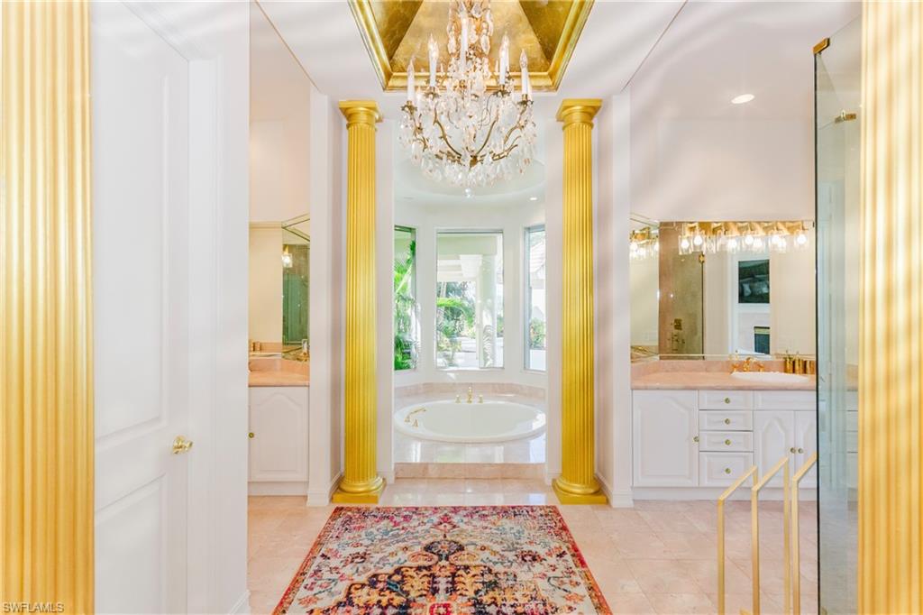 Bathroom featuring tiled bath, vanity, an inviting chandelier, a tray ceiling, and ornate columns