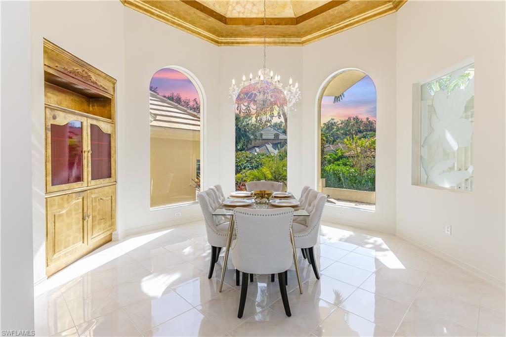 Tiled dining area with a raised ceiling, a chandelier, a towering ceiling, and ornamental molding