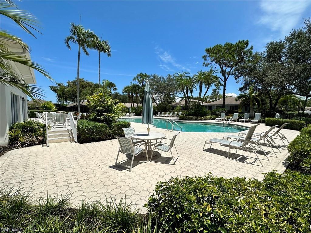 Spacious paver patio with a swimming pool, surrounded by mature landscaping and palm trees