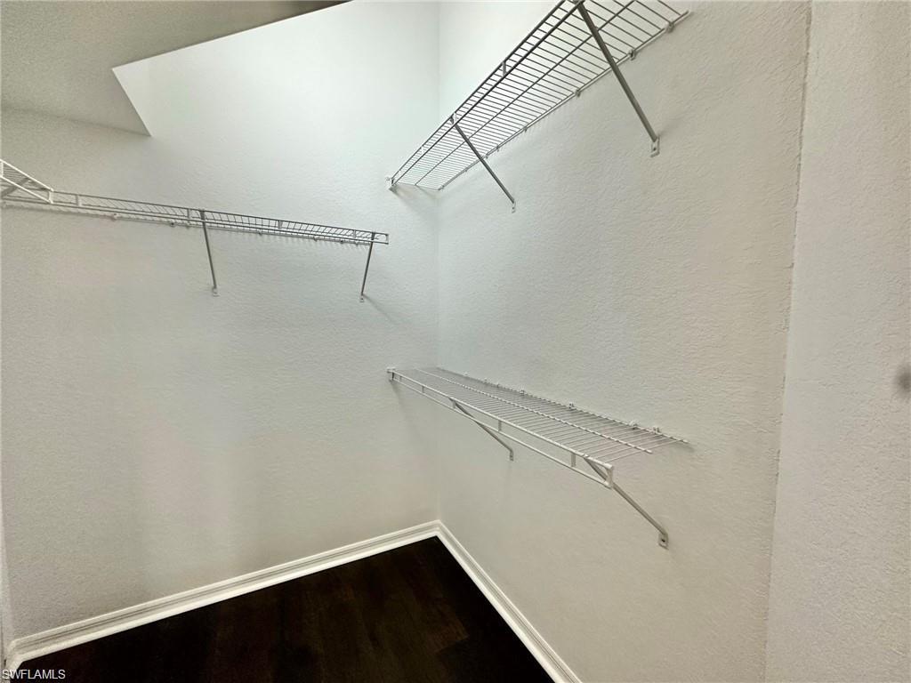 Interior closet space featuring dark wood-finish flooring, white baseboards, and multiple wire shelving units