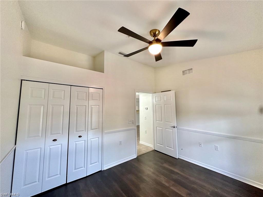 Interior room featuring wood-finish flooring, white walls with wainscoting, and a ceiling fan with integrated lighting