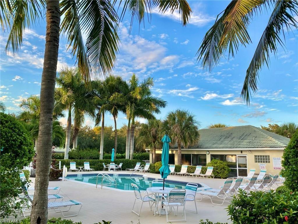 Resort-style swimming pool with integrated spa featuring a surrounding paver deck, mature palm landscaping, and a nearby clubhouse with a tiled roof