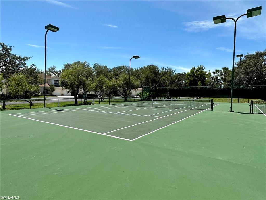 Tennis court featuring a green playing surface, perimeter fencing, and overhead lighting fixtures