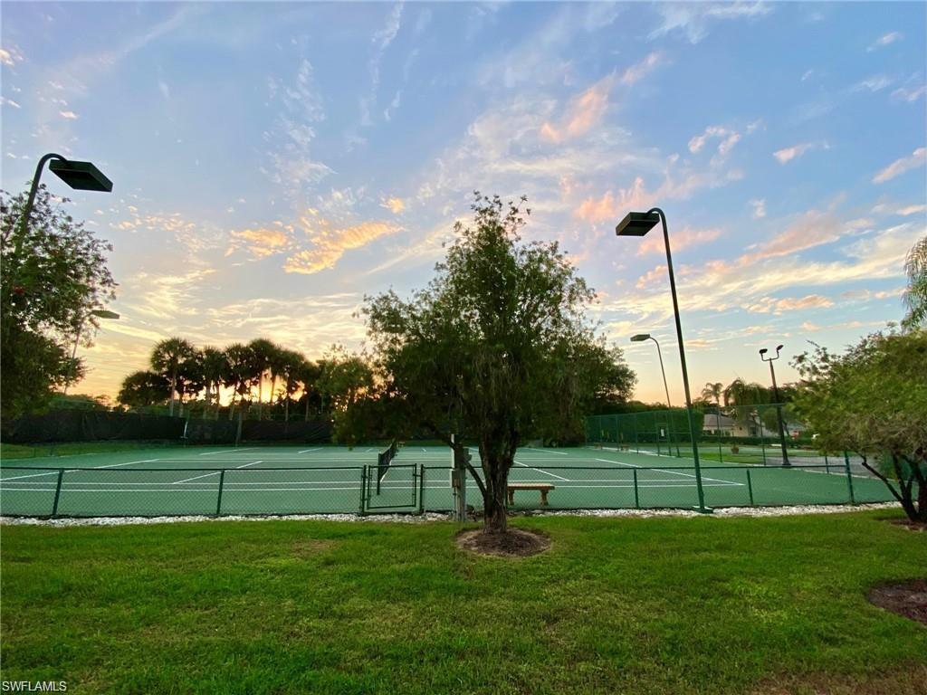 Tennis court with green surfacing, surrounded by fencing and lush landscaping