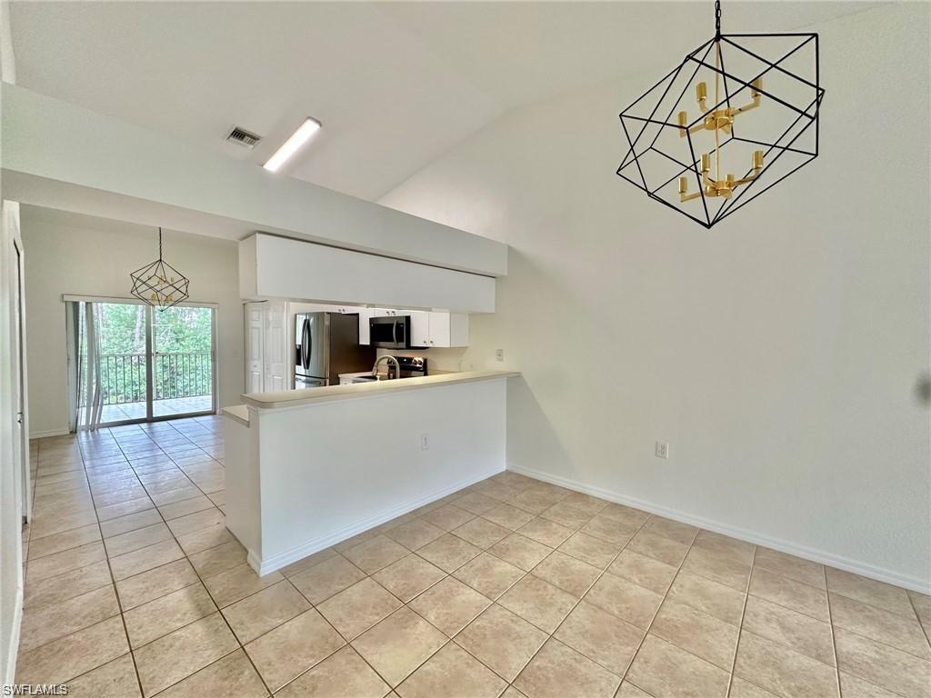 Open-concept living area featuring vaulted ceilings, tile flooring, and a contemporary geometric chandelier