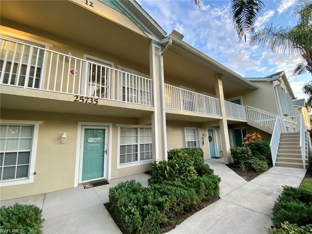 Multi-story stucco exterior featuring a ground-level entrance with a teal door and an upper-level balcony with white railings