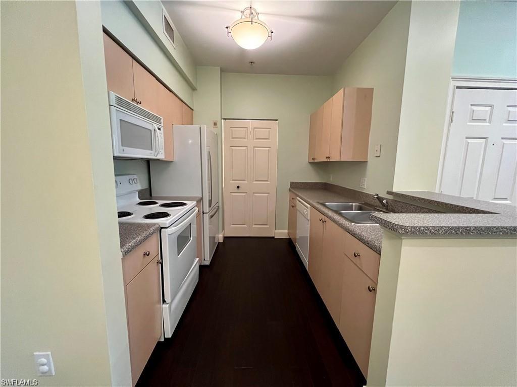 Kitchen featuring light brown cabinetry, white appliances, a sink, and laundry room