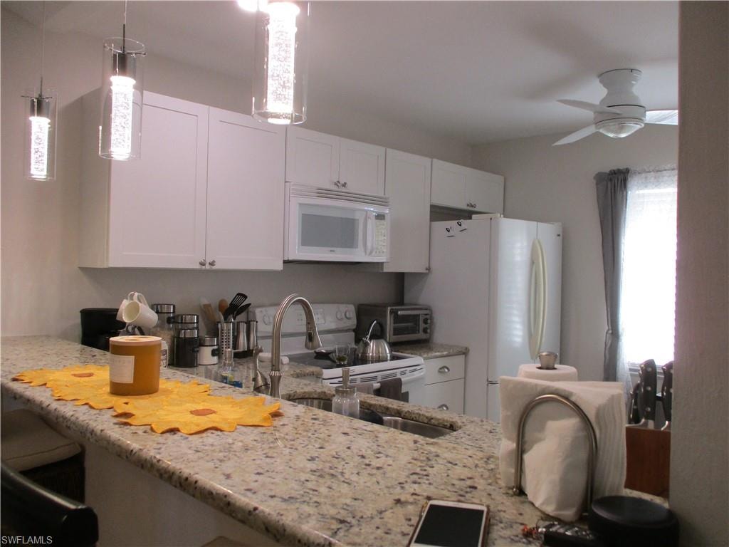 Kitchen with white appliances, a sink, light stone counters, and ceiling fan