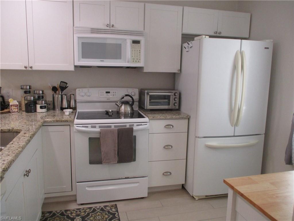 Kitchen featuring white cabinetry, light stone counters, and white appliances