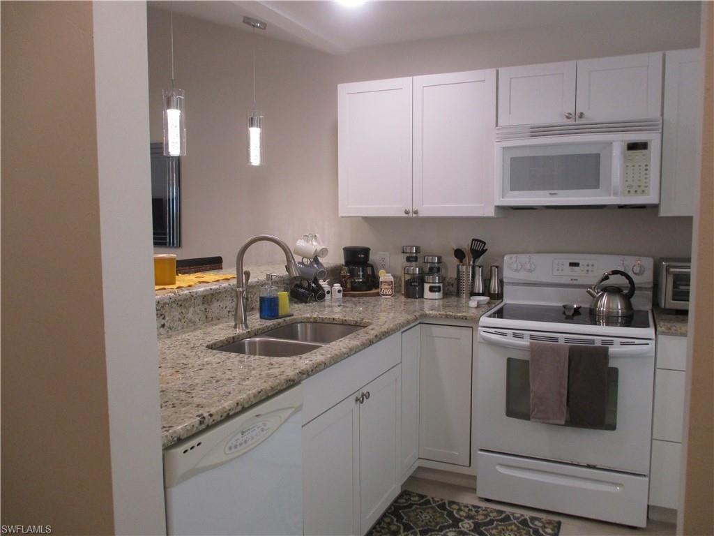Kitchen featuring light stone counters, a sink, white cabinetry, white appliances, and decorative light fixtures