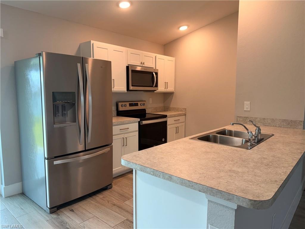 Contemporary kitchen featuring stainless steel appliances, white cabinetry, a double basin sink, light-toned countertops, and wood-finish flooring