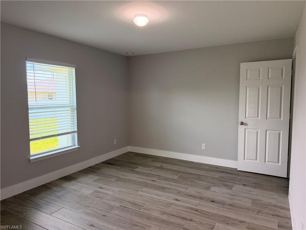 Neutral-toned room featuring wood-finish tile flooring, a multi-pane window with horizontal blinds, a ceiling-mounted light fixture, and a paneled interior door