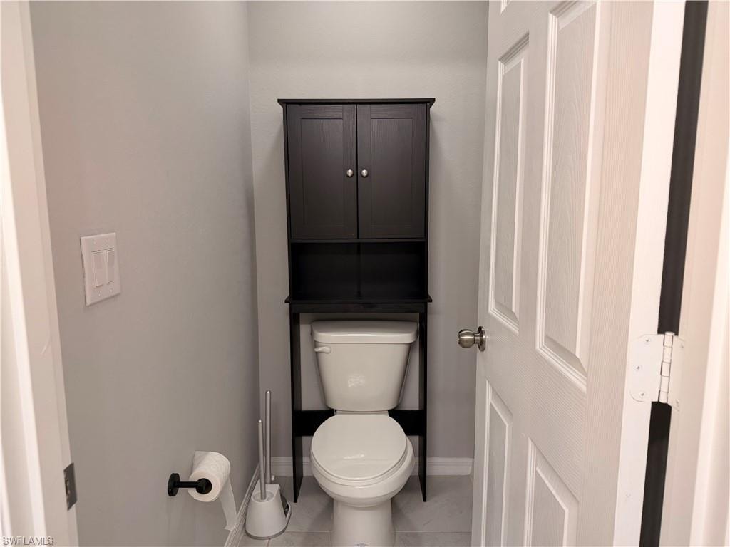 Bathroom featuring a white toilet with a black over-the-toilet storage cabinet, light gray walls, and light gray tile flooring