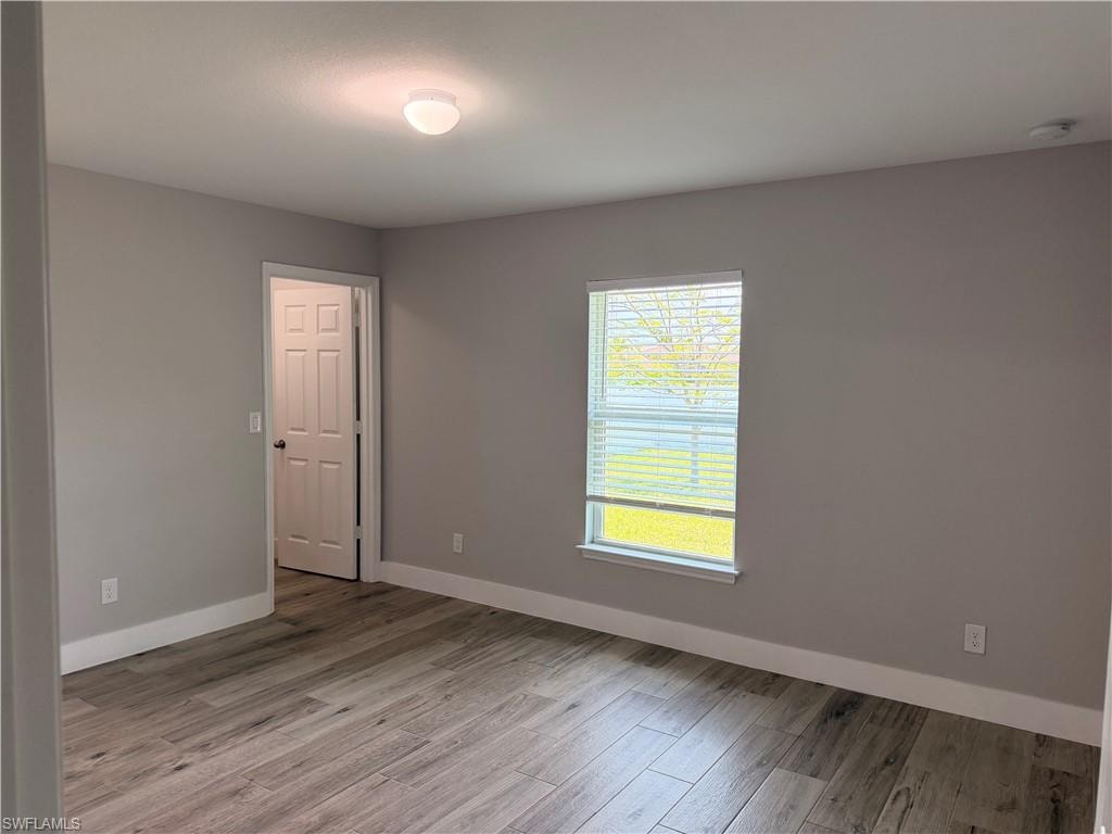 Interior room featuring wood-finish flooring, neutral wall paint, white baseboards, a single window with blinds, and a paneled door