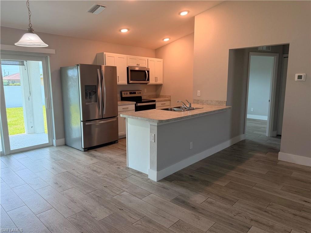 Open-concept kitchen featuring white cabinetry, stainless steel appliances, a breakfast bar, and wood-finish flooring