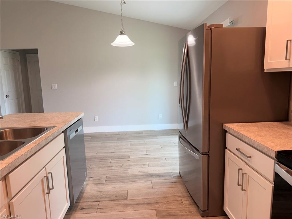 Kitchen featuring light wood-finish tile flooring, white shaker-style cabinetry with chrome pulls, stainless steel appliances including a refrigerator and dishwasher, and a double basin stainless steel sink