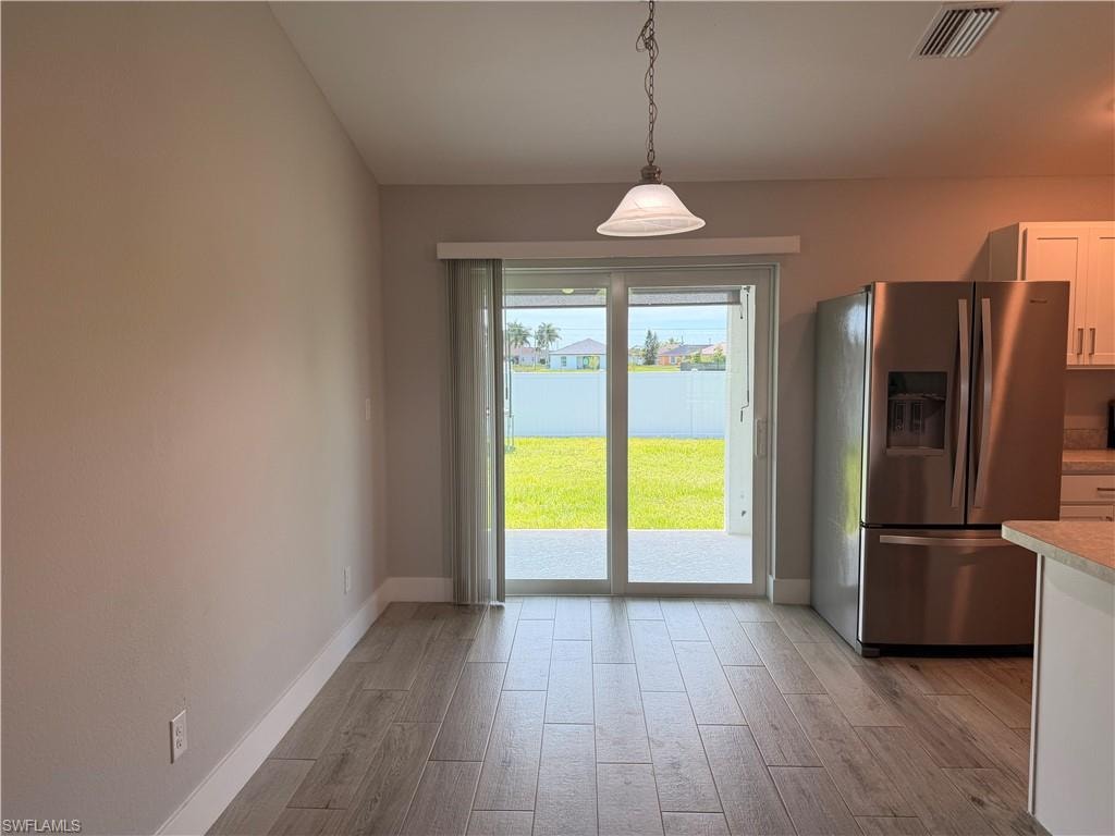 Dining area featuring wood-finish flooring, a contemporary pendant light fixture, and sliding glass doors opening to a concrete patio