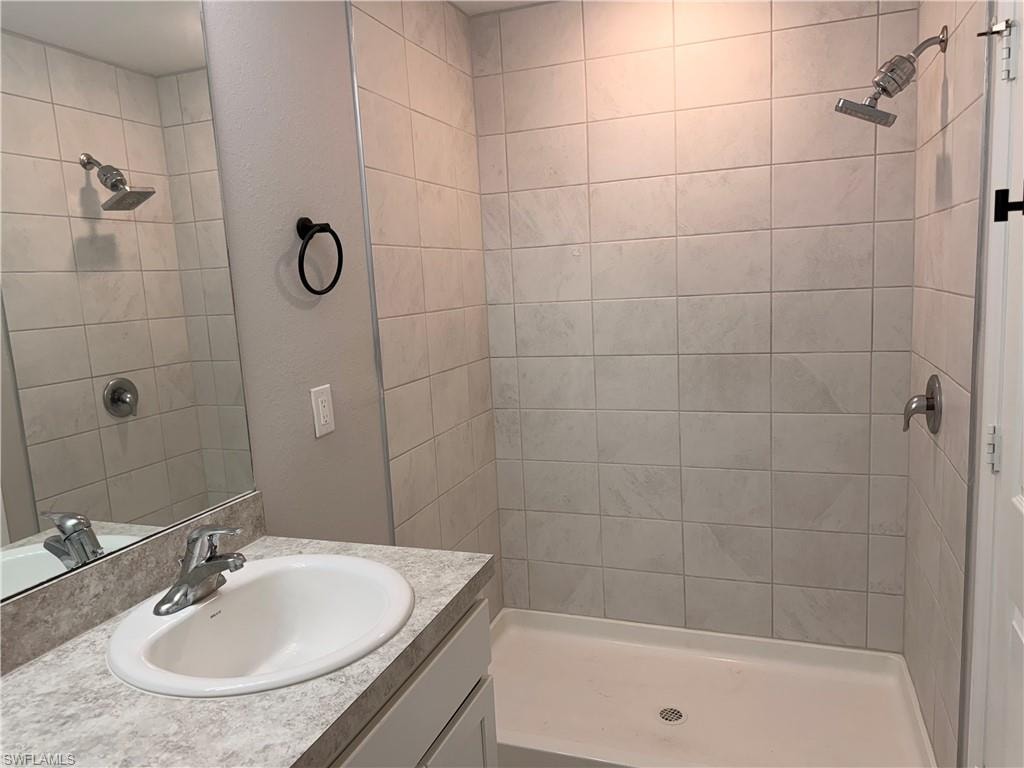 Bathroom featuring a walk-in shower with light-toned rectangular wall tiling, a rainfall showerhead, and a vanity with an integrated sink and laminate countertop