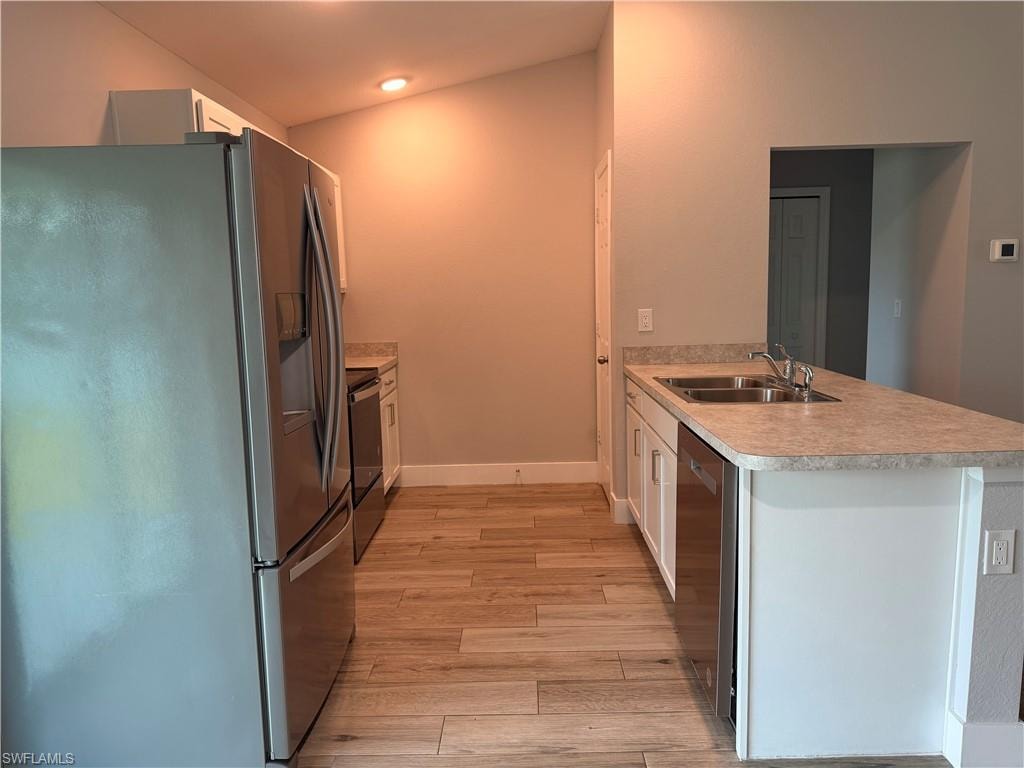 Kitchen featuring wood-finish flooring, stainless steel appliances, white cabinetry, a double basin sink, and a breakfast bar