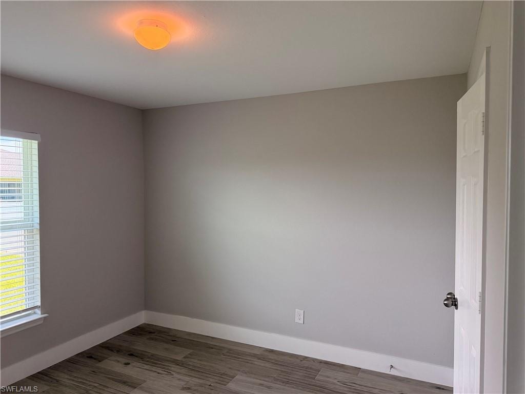 Room featuring wood-finish flooring, neutral wall paint, white baseboards, and a window with blinds